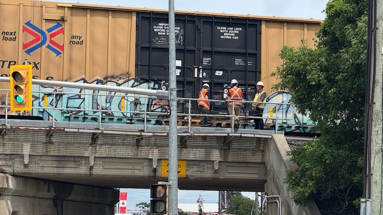Workers in safety vests sand on a bridge where there's a stopped train