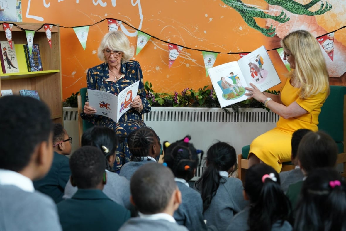 Two adults hold up books as they read to several children seated on the floor in front of them.