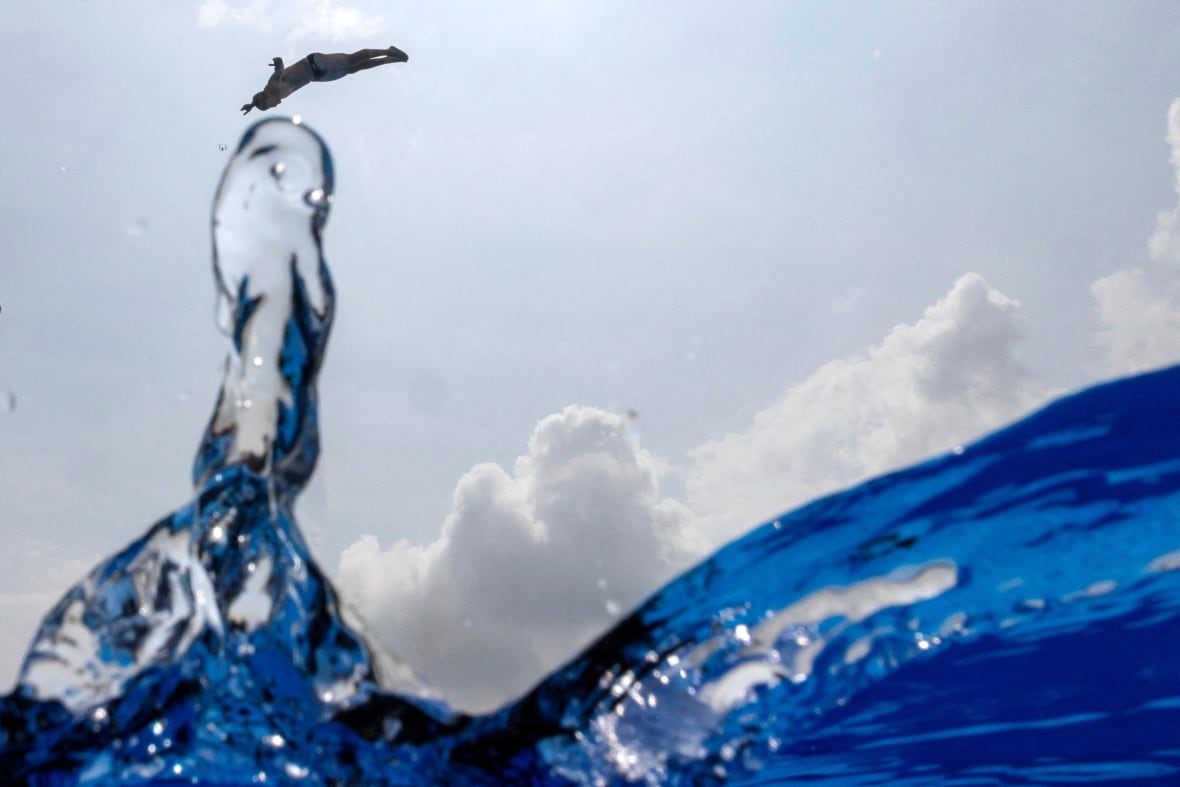 A man dives into a pool against a cloudy sky.