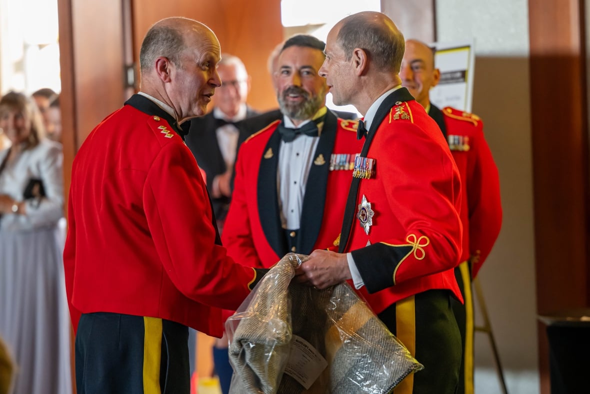 A person holding a blanket shakes hands with another person as others look on.