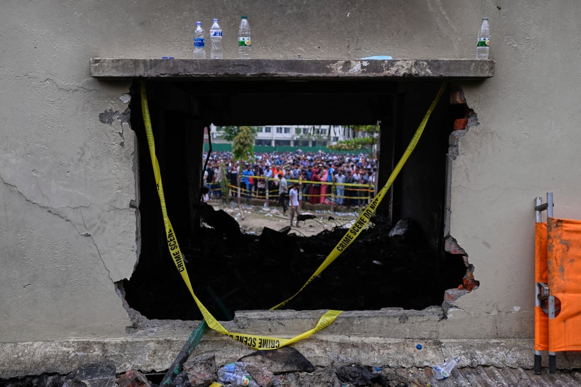 A crowd is pictured through a hole in a concrete wall with yellow tape dangling across it.