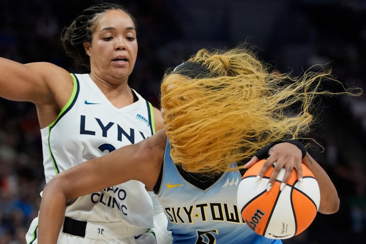 A woman dribbles an orange and white basketball as her blonde hair crosses her face.