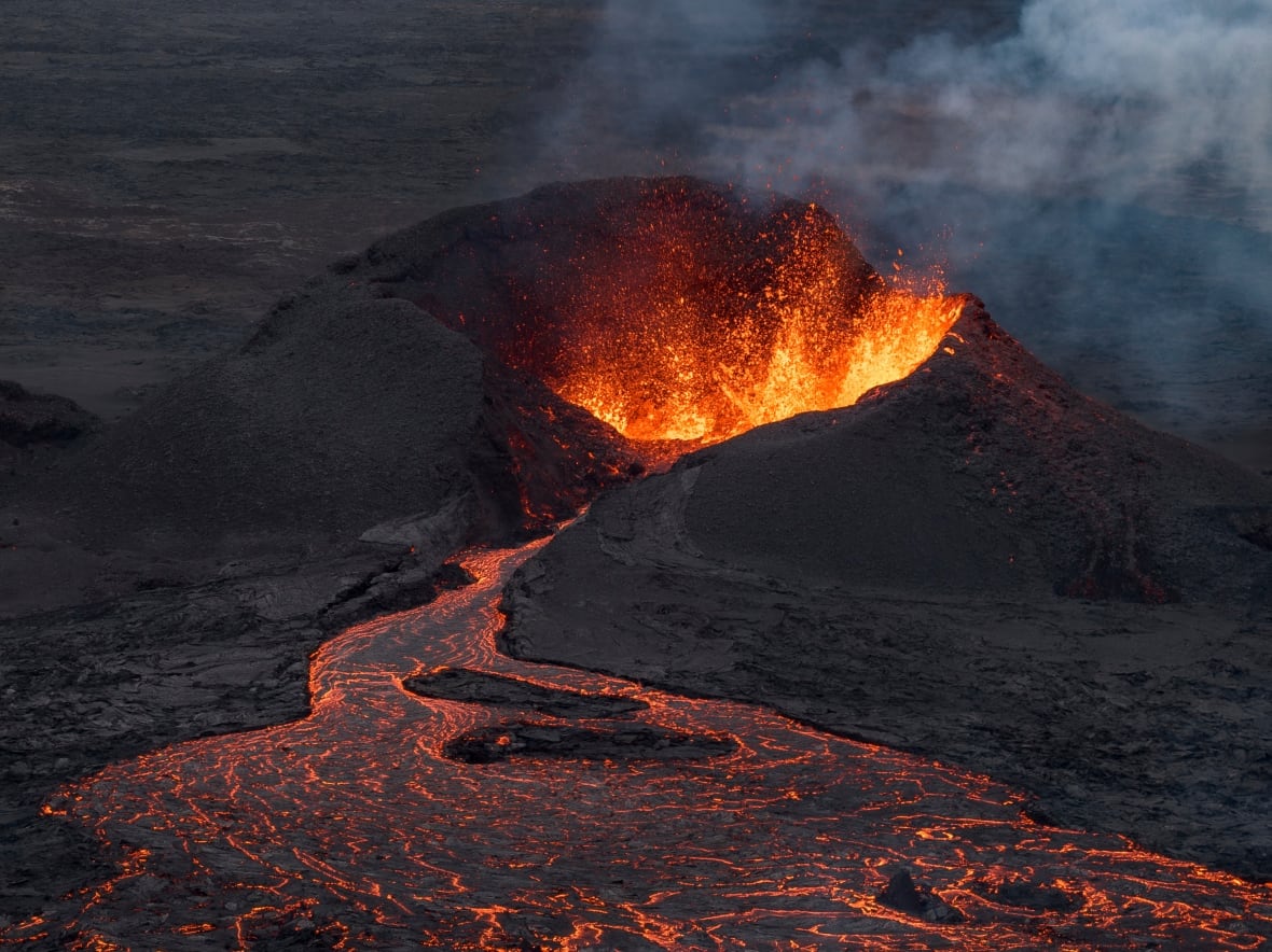 Red and orange lava flows out of a dark cavern.
