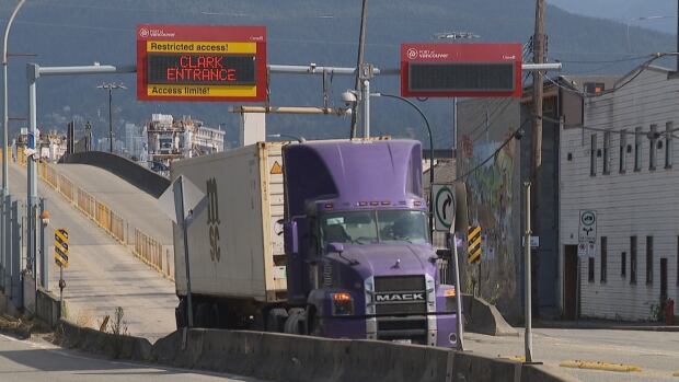 A purple truck hauling a white container drives out of the Port of Vancouver on the Clark Drive off ramp.