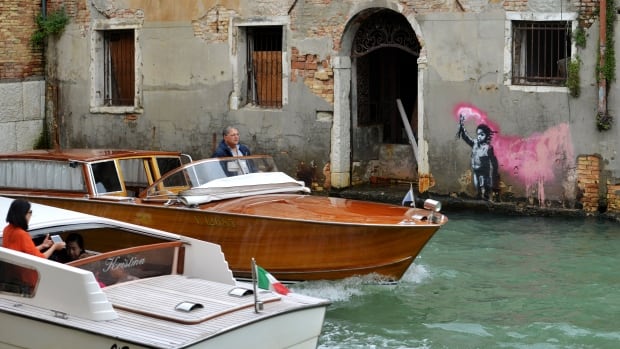 Motorboats pass in front of an alleged work by British street artist Banksy on the outer wall of a building overlooking a canal in Venice.