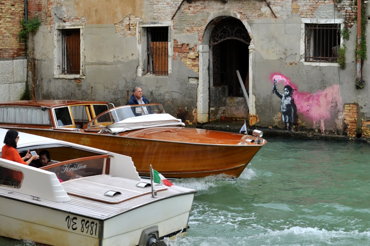 Motorboats pass in front of an alleged work by British street artist Banksy on the outer wall of a building overlooking a canal in Venice.
