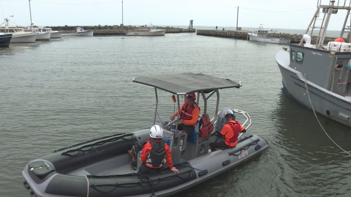 An inflatable boat with three people aboard wearing reflective orange clothing.