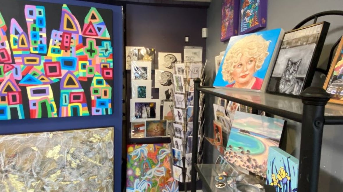 Colourful art pieces on a purple moving sectional wall stand beside racks of art prints on glass shelves
