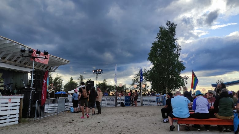 An outdoor stage with a moderately dark cloud over it. There are people sitting in picnic tables to the right.