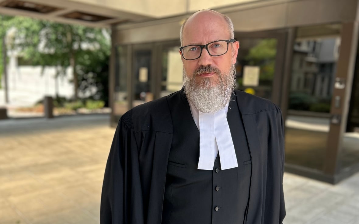 A man in robes stands outside a courthouse.