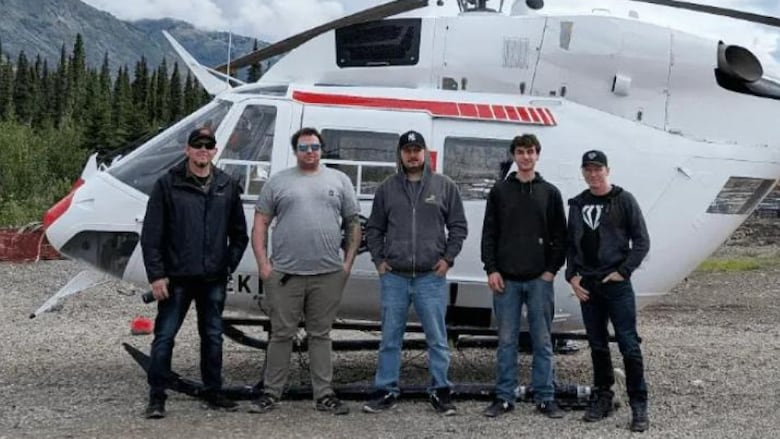 Five men stand in front of a helicopter