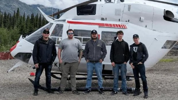 Five men stand in front of a helicopter