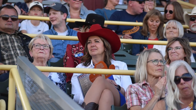 A woman in a red cowboy hat sits in a full grandstand watching a rodeo.