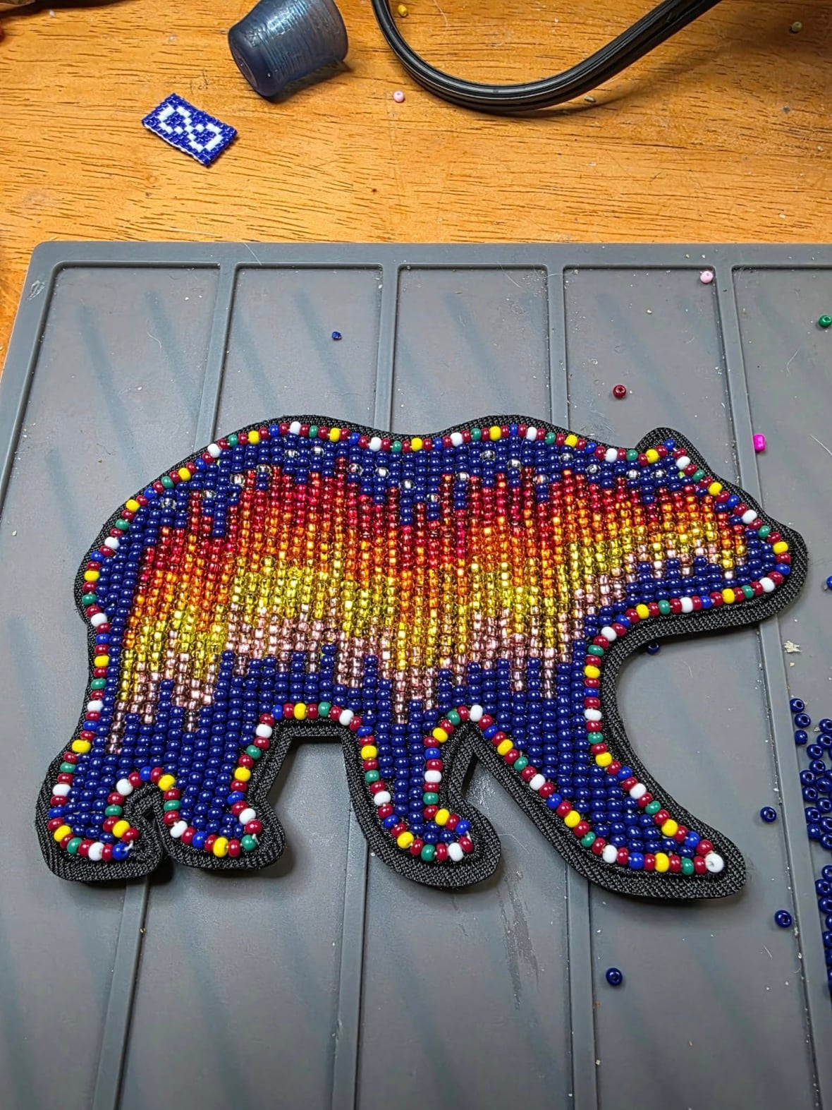 A beaded bear in the bright colors sits on a table.