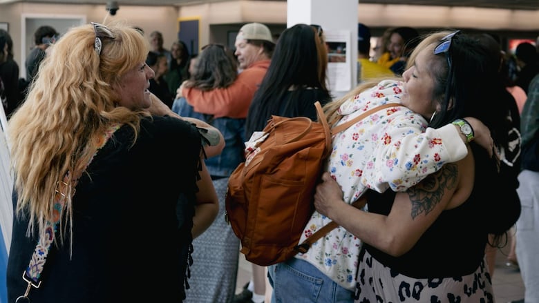 Airport waiting area, many people inside and hugging each other and catching up.