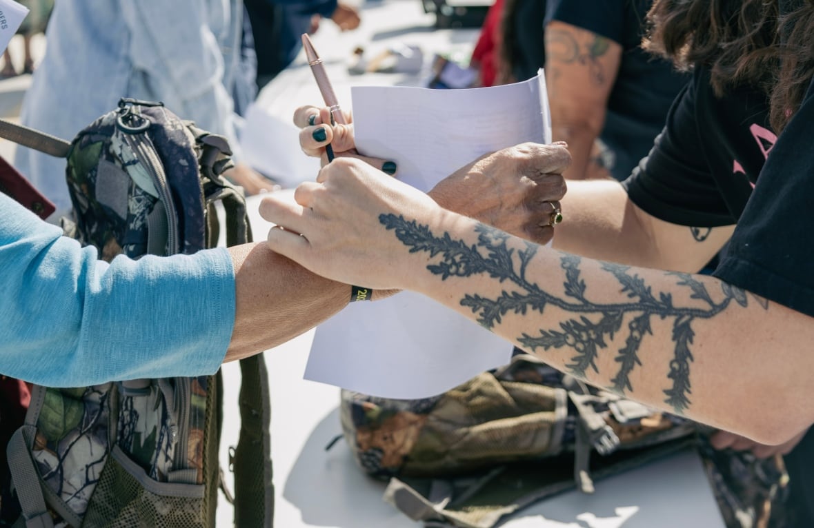 Two hands. One helps put a ribbon bracelet on another woman.