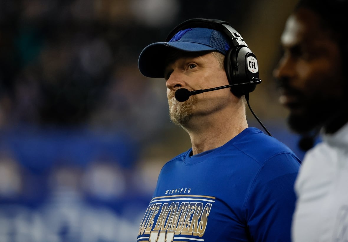 A man in a blue shirt and baseball cap looks ruefully while wearing a headset.