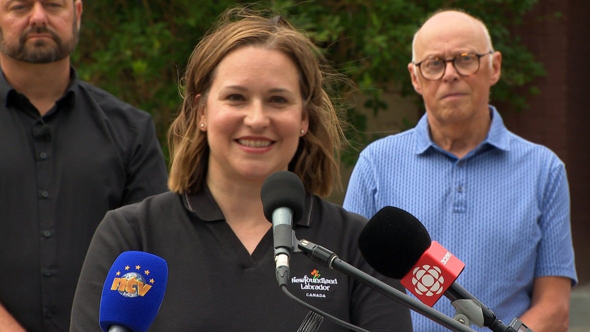 A woman with brown hair smiles, standing behind a podium.