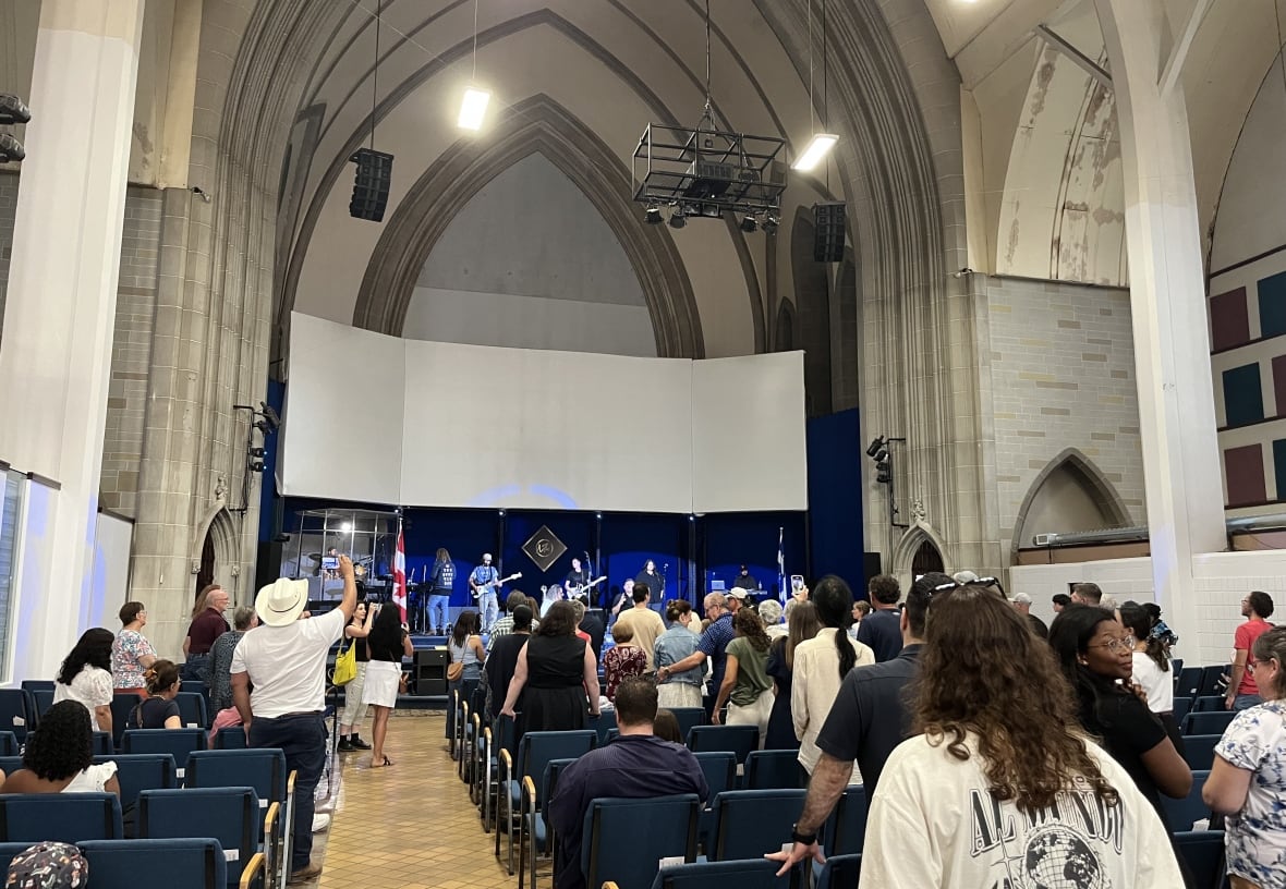 Los músicos aparecen en un escenario dentro de la iglesia, los fieles se sientan o se paran cuando los miran.