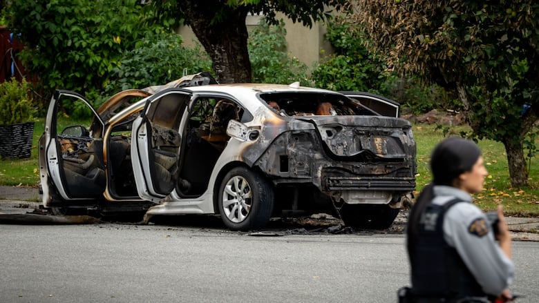 A police officer stands near a burned vehicle.