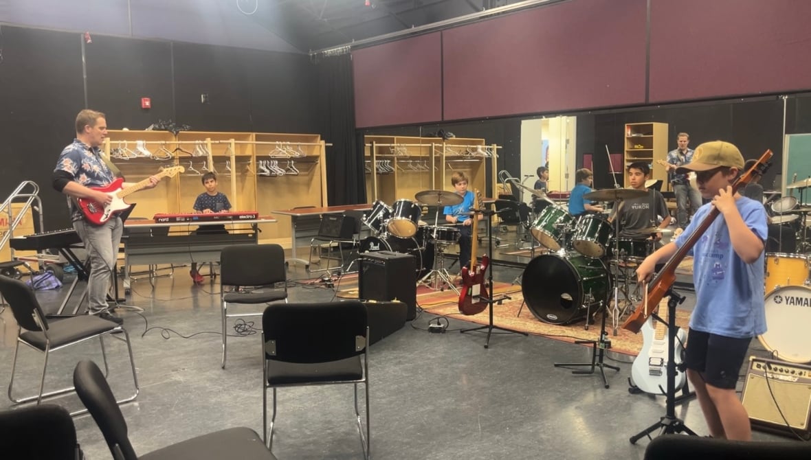 Kids playing instruments led by an adult man on electric guitar.
