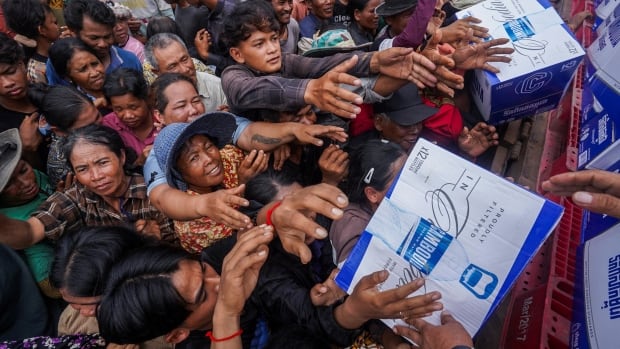 A large crowd of people reaches out to receive aid.
