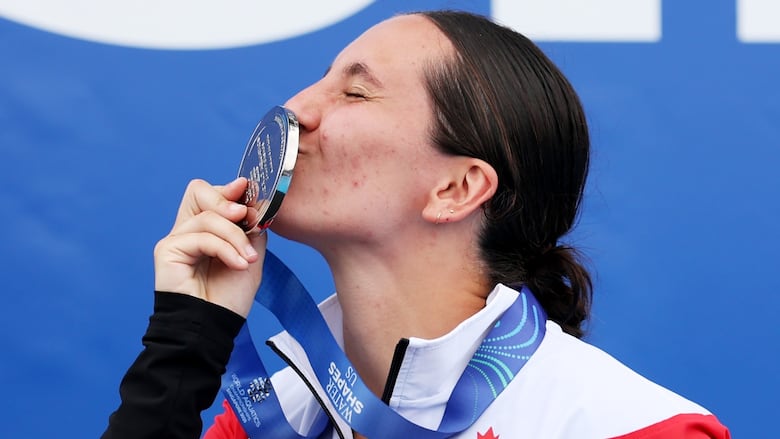 A woman is shown at profile closing her eyes and kissing a silver medal.