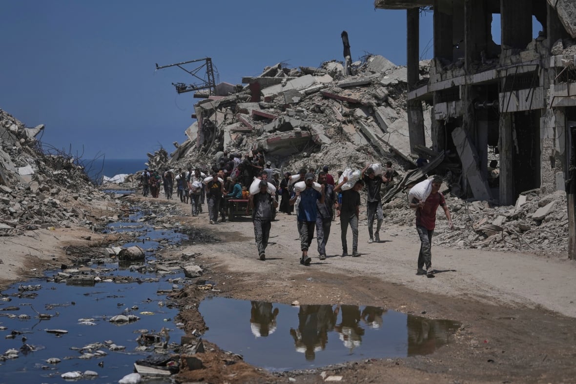 People carry sacks of flour as they walk past destroyed buildings.