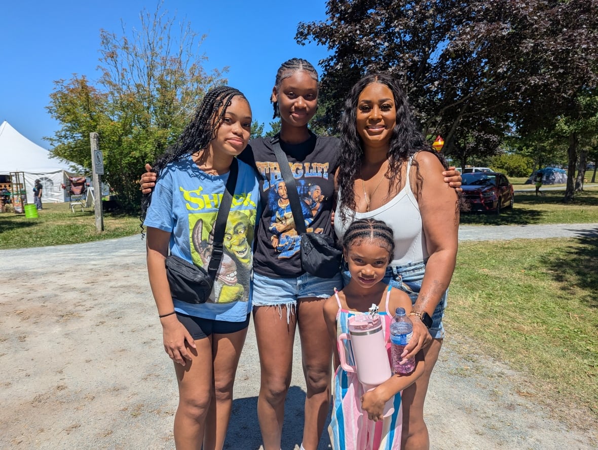 Three sisters with their mom pose for a picture outside.