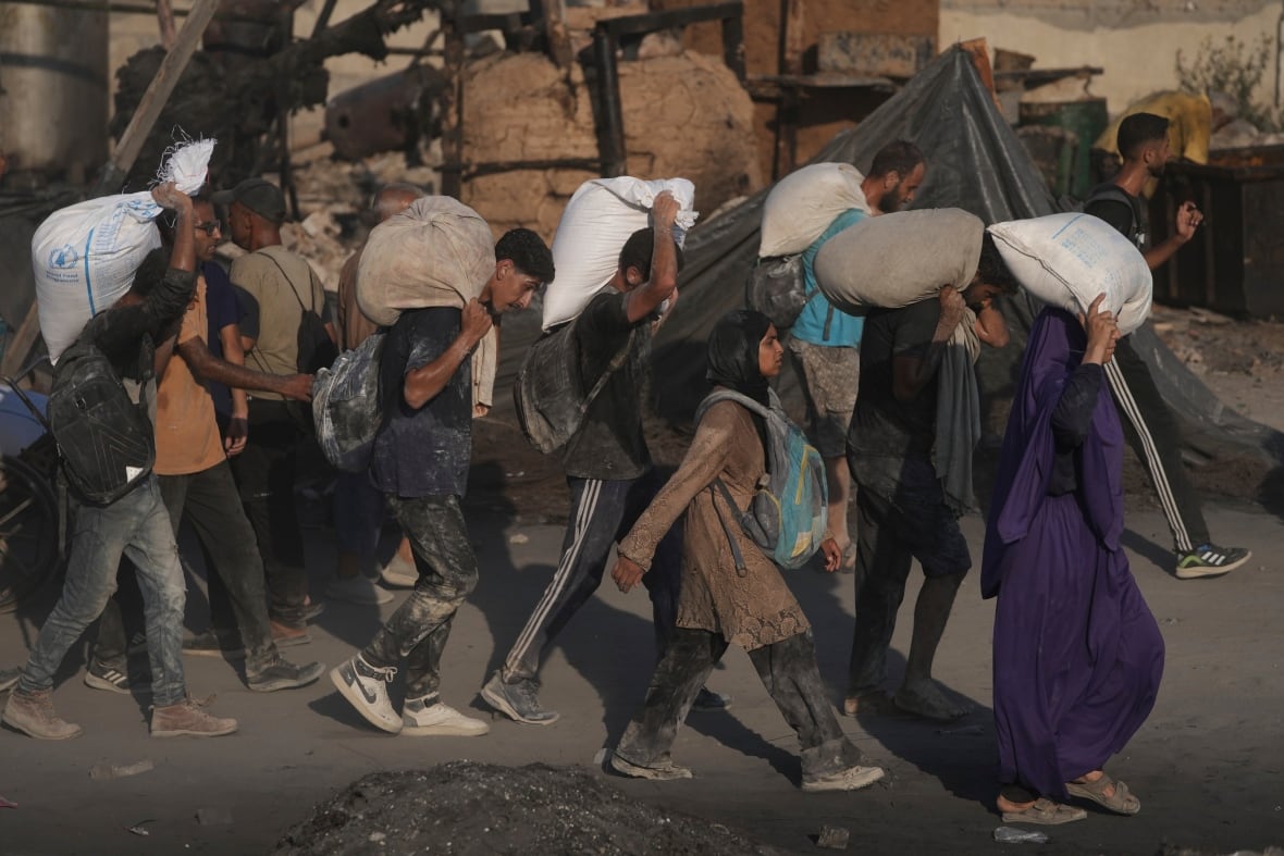 People carry sacks of flour past destroyed buildings.