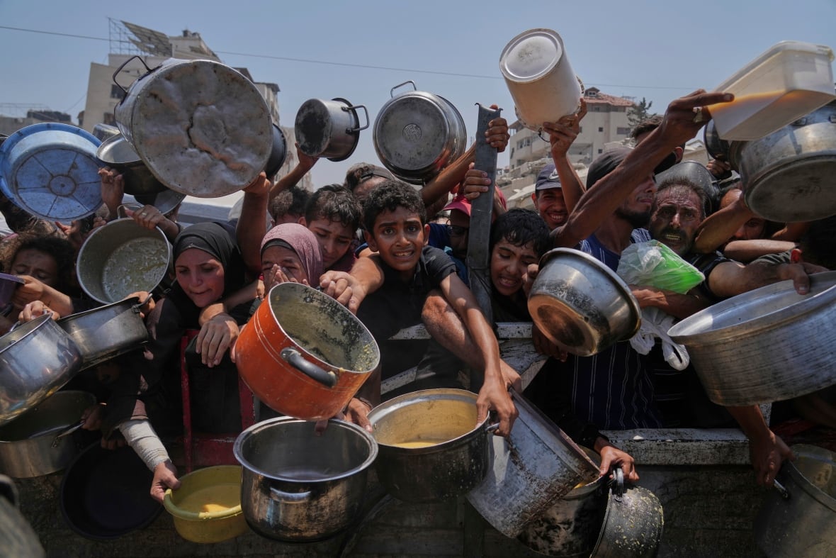 People desperately stretch out with their pans and other containers for food at a distribution site.