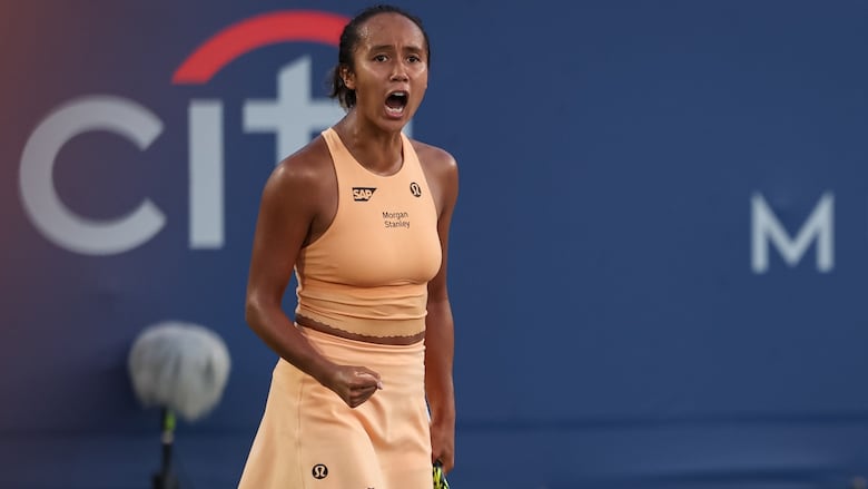 A female tennis player pumps her right fist while yelling in celebration on the court.