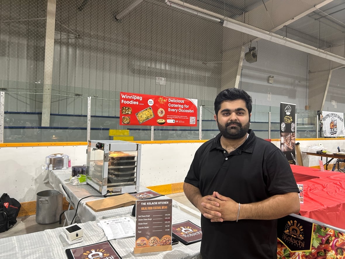 Man with dark hair wears a black t-shirt and stands infront of a food stall inside a hockey arena