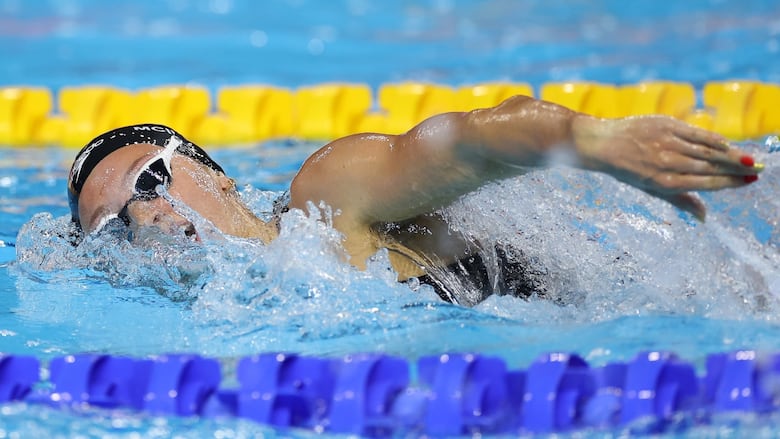 Water splashes around a female swimmer who is taking a breath while competing in a freestyle race.