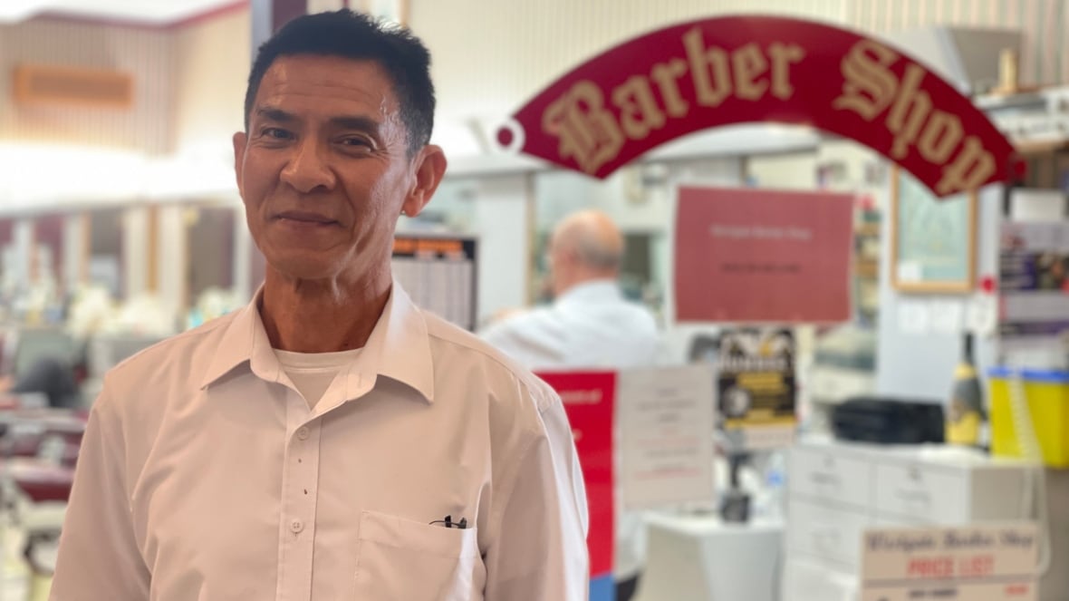 A man in a white shirt stands in front of a barber shop.