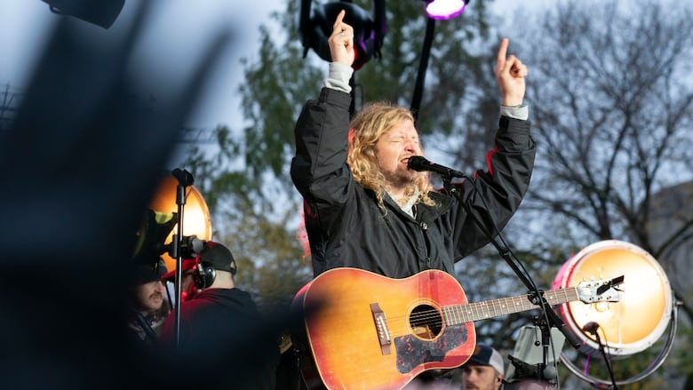 A man with a guitar closes his eyes and puts his arm to the sky.