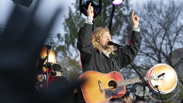 A man with a guitar closes his eyes and puts his arm to the sky.