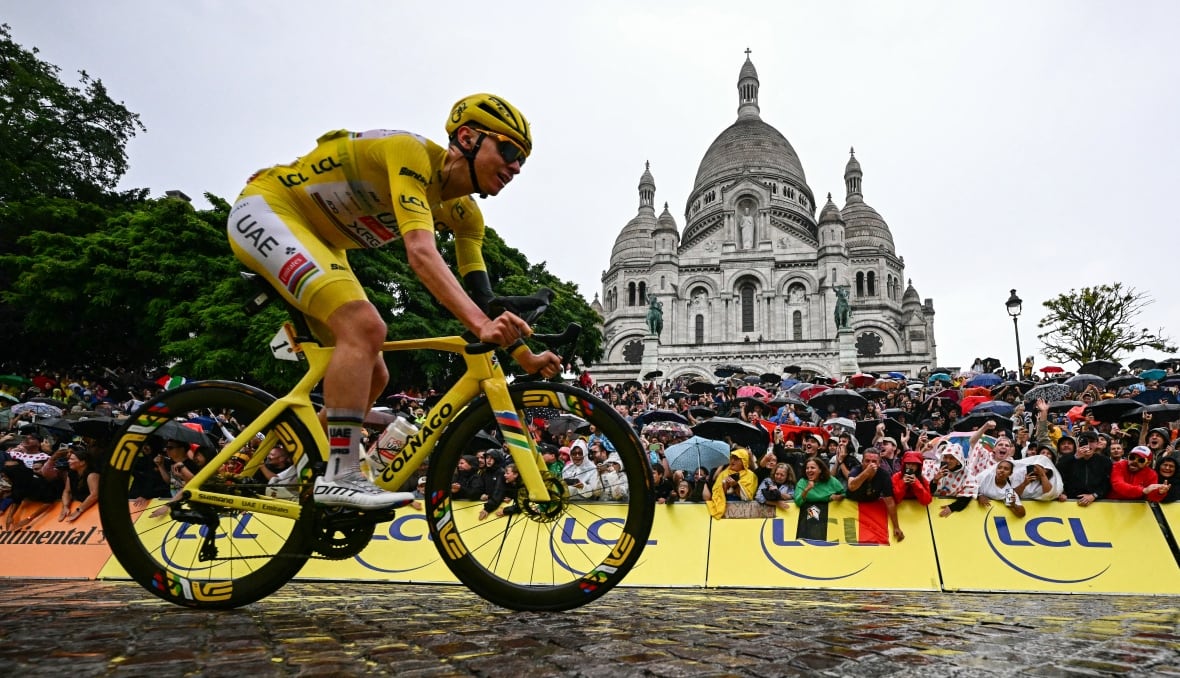 Um ciclista vestindo a camisa amarela do líder passa de bicicleta pela Basílica do Sagrado Coração, em Paris.