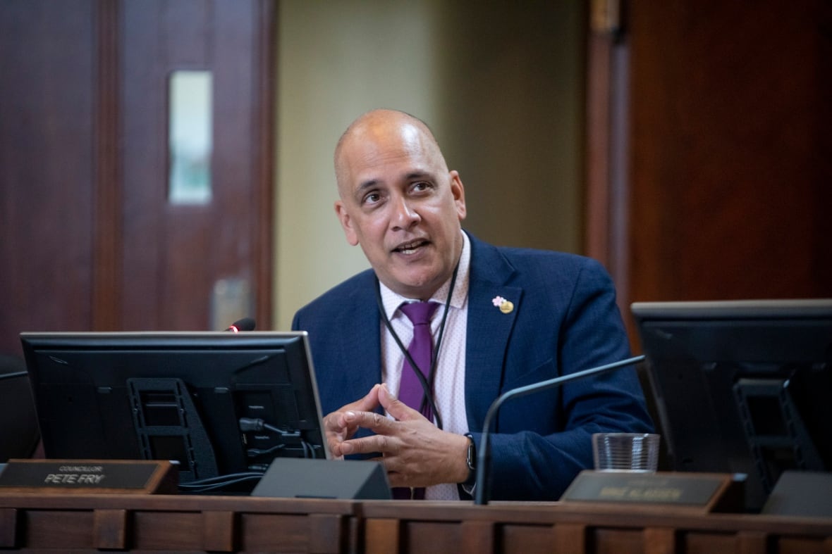 A Black man speaks in council chambers.