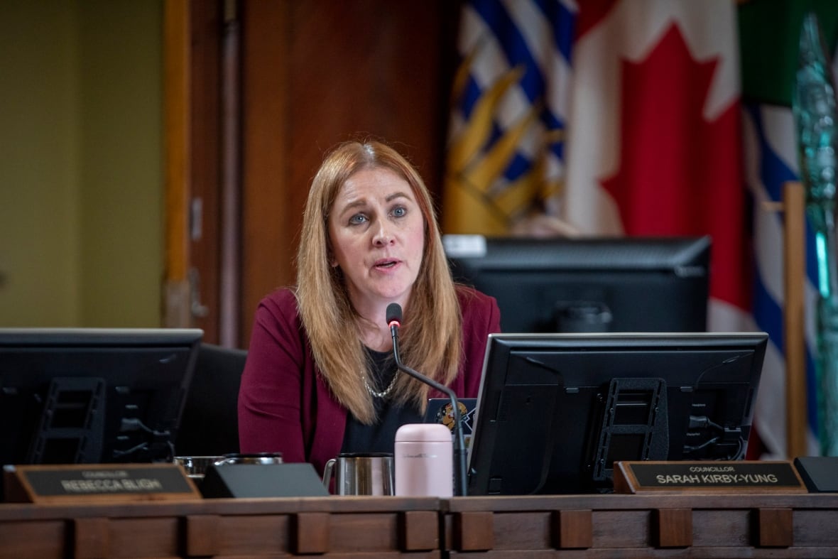 A blond woman speaks in council chambers.