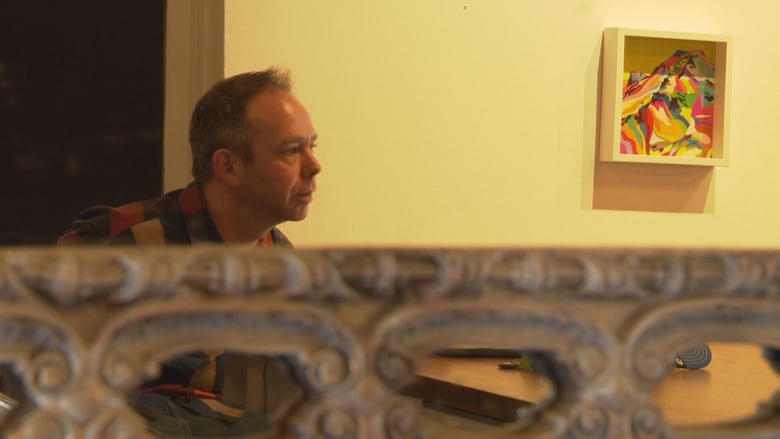 A man looks past a painting in a gallery.