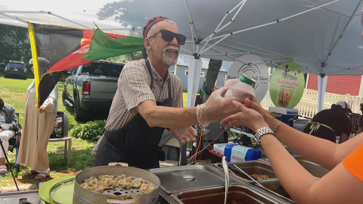 A man wearing sunglasses and an apron hands a can over to a woman in an orange shirt.