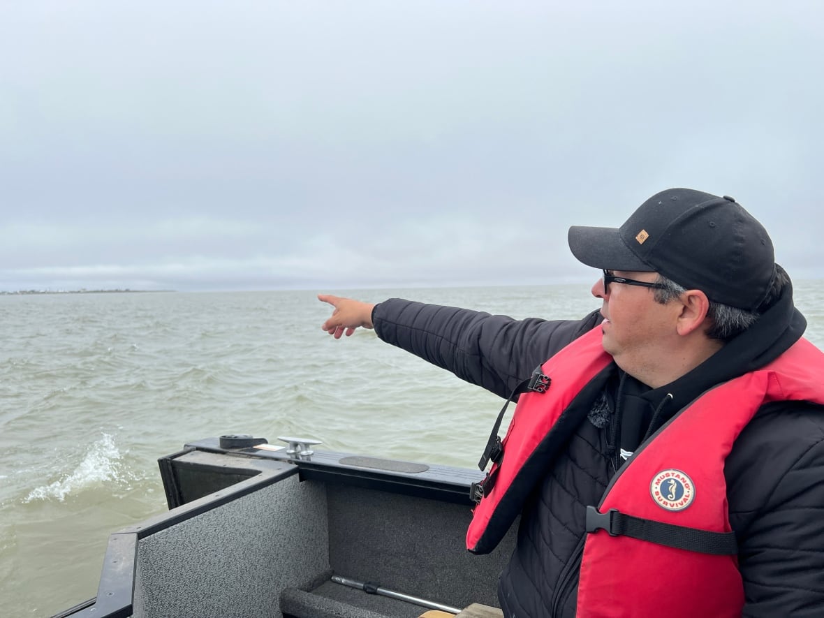 A man on a boat points to the shore.