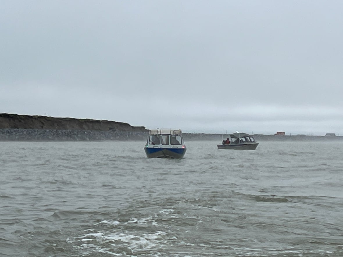 Two boats sit on the ocean near the shore of Tuktoyaktuk.