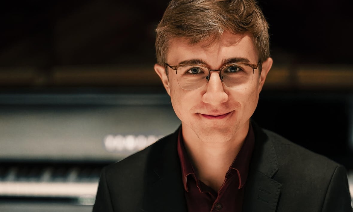 Samuel Lauzon-Schnittka, wearing a black suit, faces the camera with a grand piano behind him.