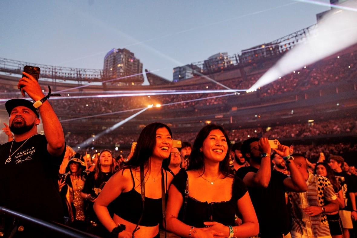 Una pareja de mujeres sonrientes se encuentran frente a una gran multitud detrás de ellas.