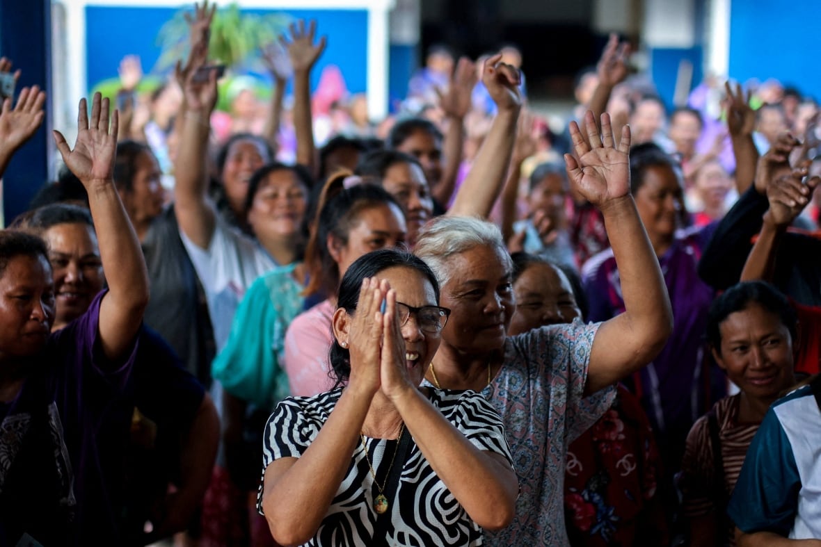 A crowd of people cheers inside a temporary shelter.