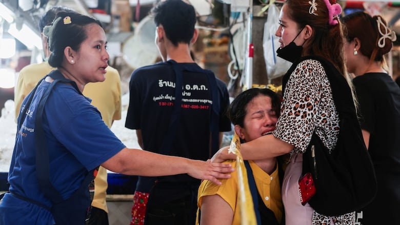 Two women console another woman who is crying at a market in Thailand.