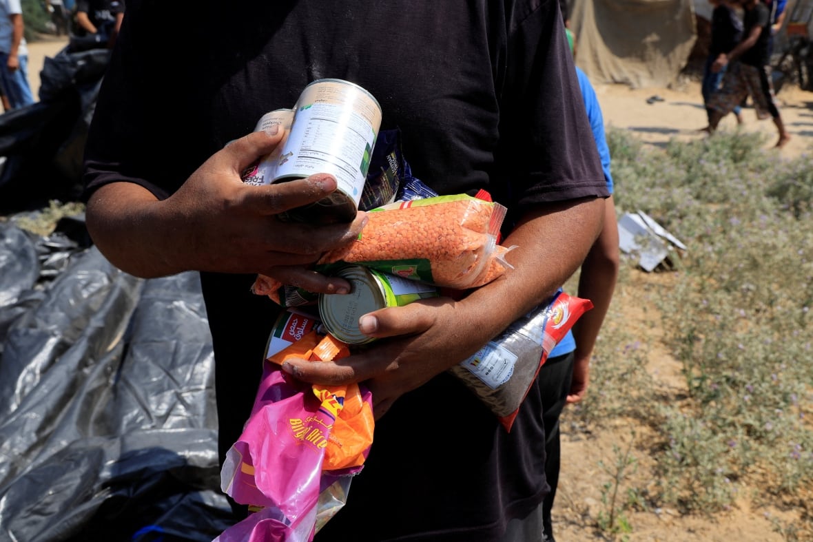 The man holds many food items.