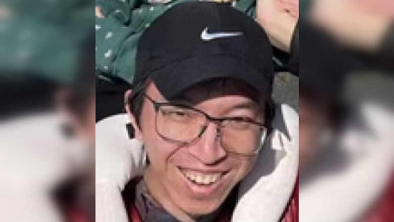 Close up of the face of a smiling man. He has eyeglasses and a baseball cap.